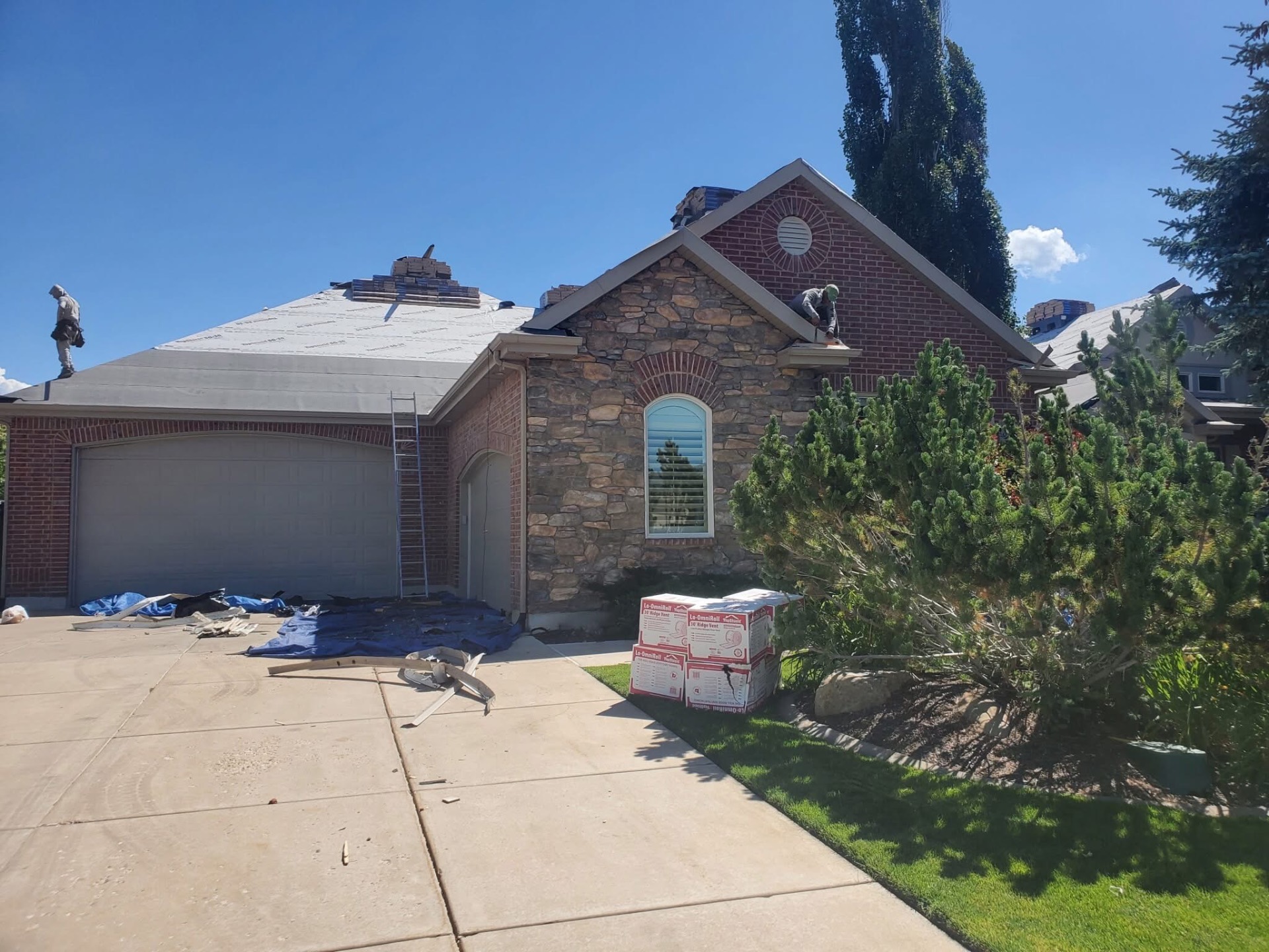 Roofers working on a stone and brick home with ridge vent materials