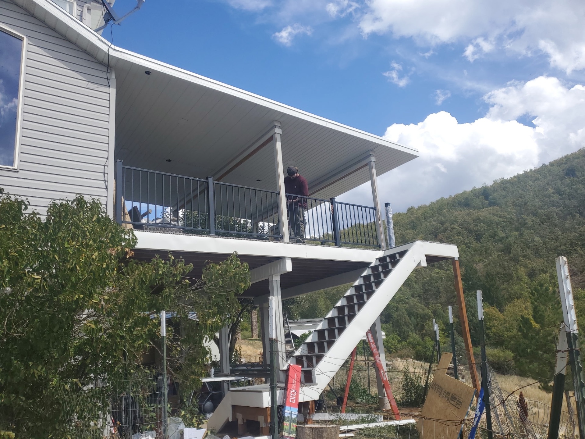 Second-story covered deck with stairs and railings in a hillside yard